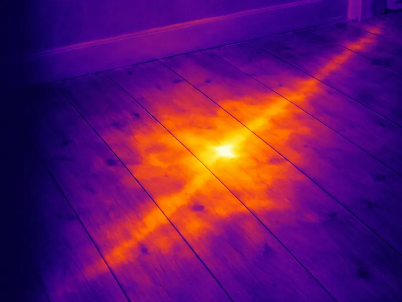 Thermal illustration of a hot water pipe leaking under floorboards, the pipe run showing through the boards